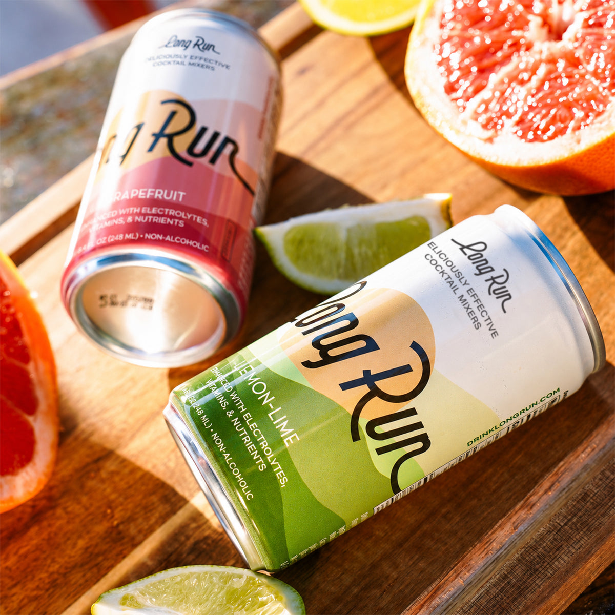 Two Long Run sparkling non-alcoholic drinks in aluminum cans, one labeled Grapefruit and one labeled ION-LIME, arranged on a wooden board with grapefruit slices and lime wedges.