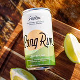 A can of Long Run Lemon-Lime cocktail mixer sits on a wooden cutting board with lime wedges around it. The can is white with green and yellow graphics and black script text.